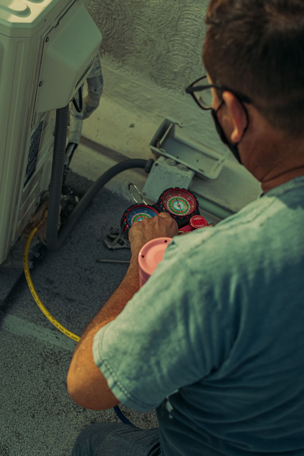 A technician servicing an outdoor air conditioning unit with gauges