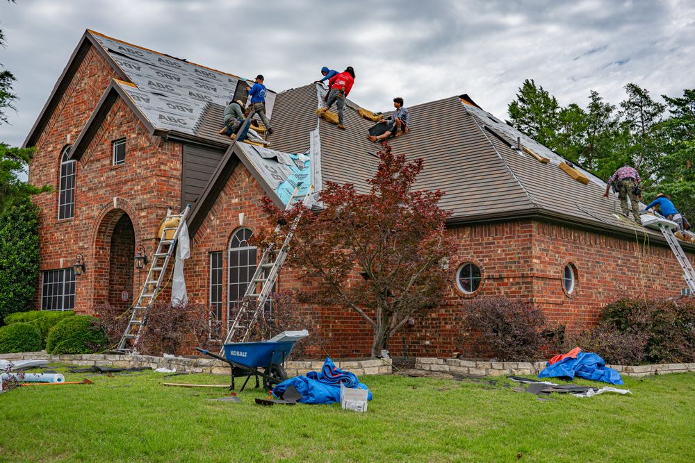 Roofers working on the shingled roof of a brick house